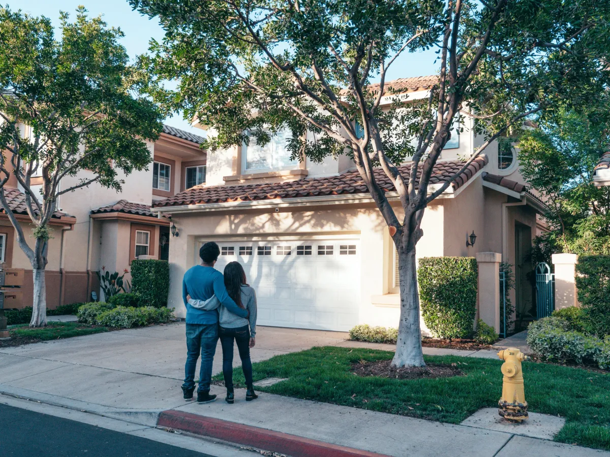 A couple standing in front of a house, smiling and holding hands.