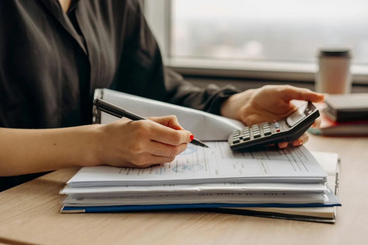 A woman's hands writing on paper with a calculator and pen, demonstrating financial calculations.