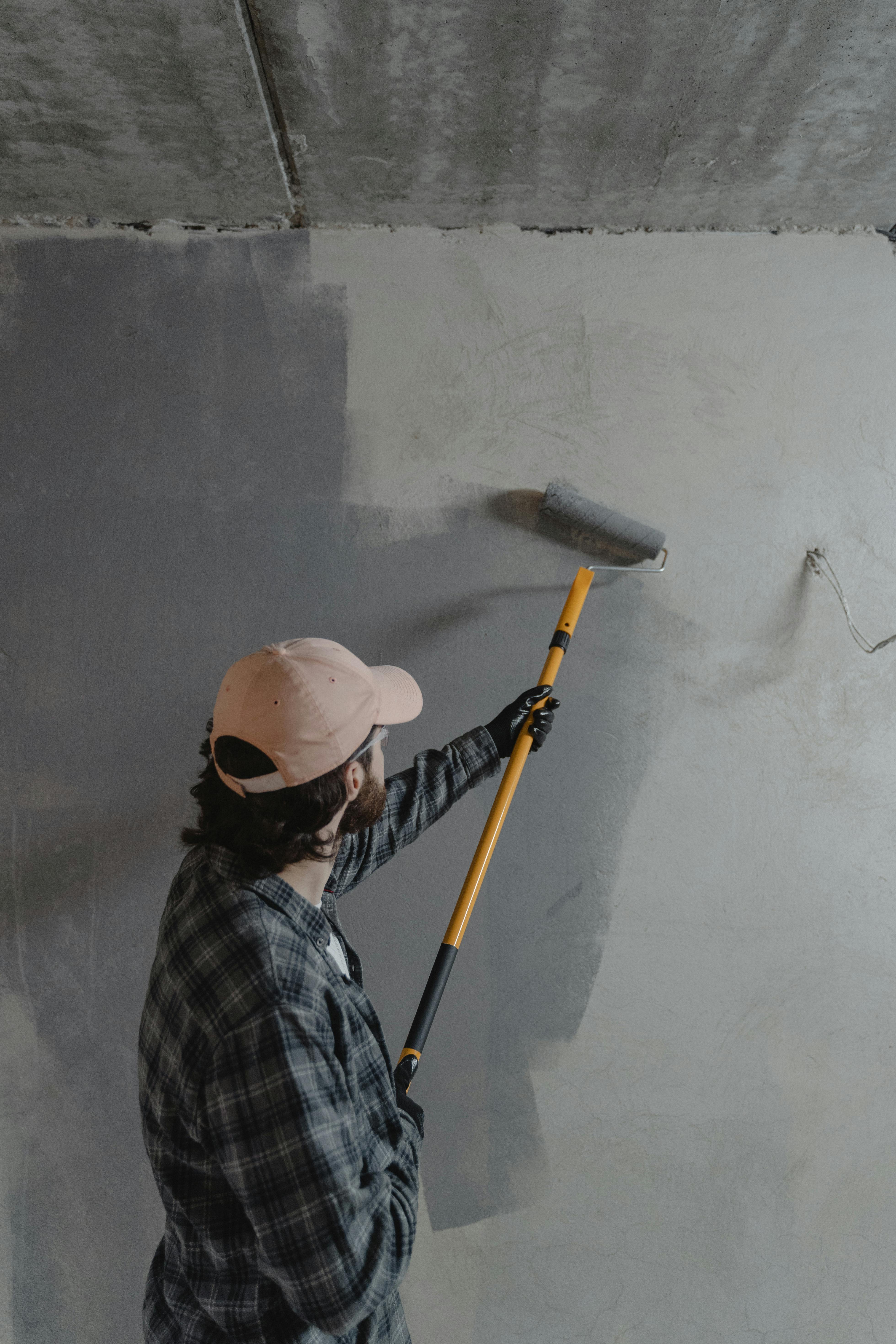 man using paint roller to paint wall grey