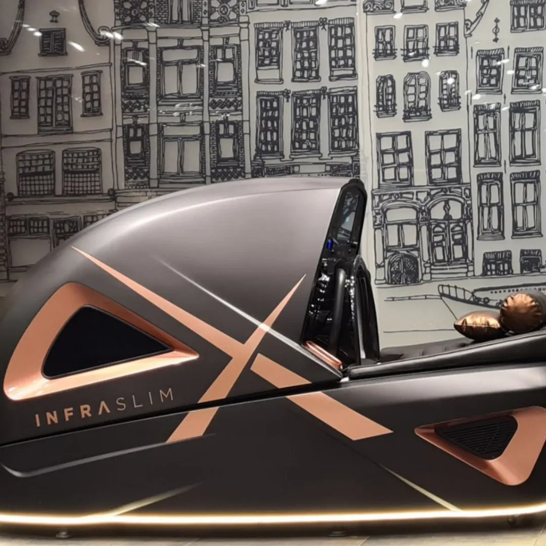 InfraslimX machine with a sleek dark gray design and rose gold accents, featuring a luxurious interior and advanced control panel, set against an illustrated backdrop.