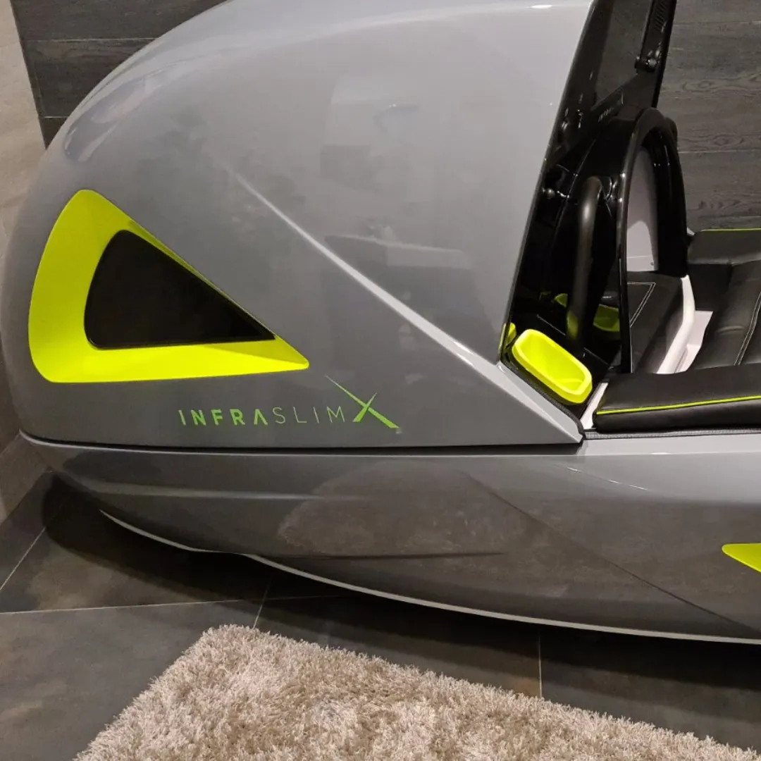 InfraslimX machine in gray with striking neon green accents, showcasing its futuristic design and sleek lines. The machine is open, displaying the ergonomic seat inside, ready for use.