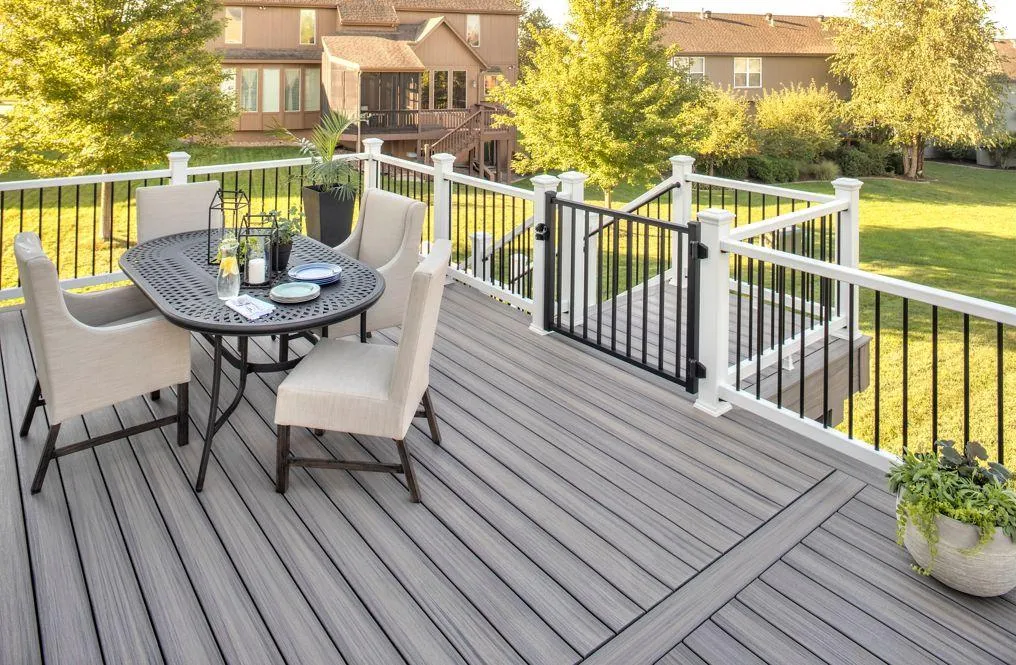 Outdoor dining set on a modern grey deck with white railing and green lawn in the background.