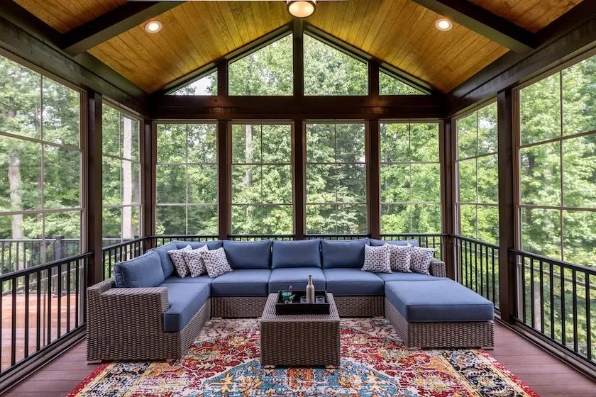 Enclosed patio with sectional sofa and panoramic forest view for cozy outdoor living space design inspiration.