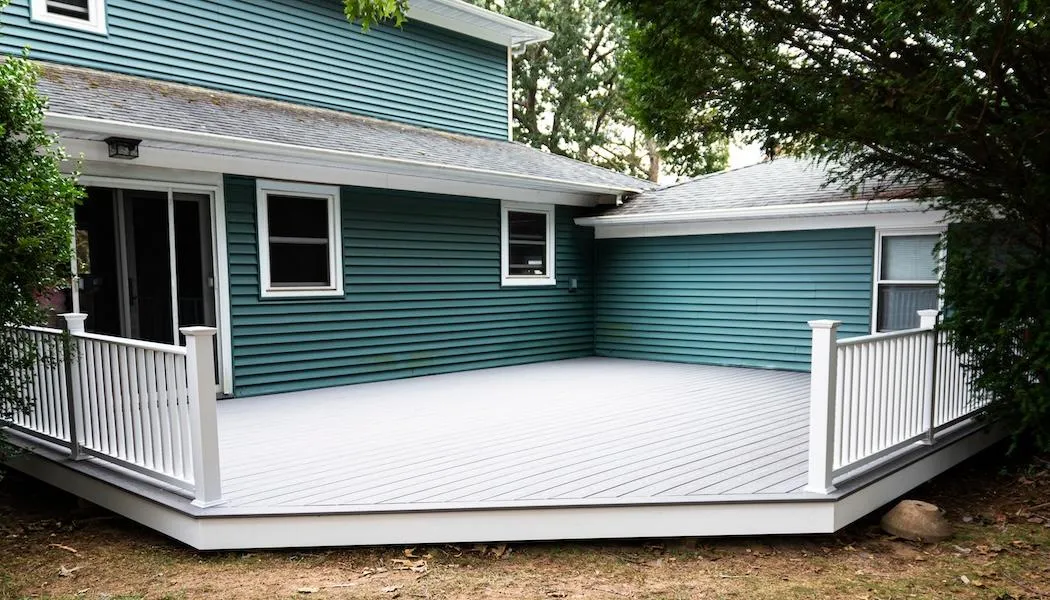 Completed elegant white and gray deck installation adjacent to a teal blue house, showcasing the seamless integration with the home's exterior.