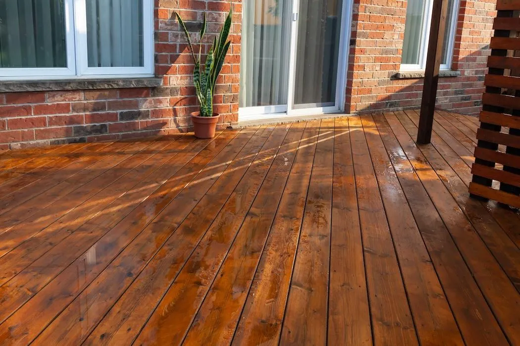 Refinished wooden deck with a rich, honey-toned stain by Skyline Decks, enhancing the cozy charm of a brick house exterior.