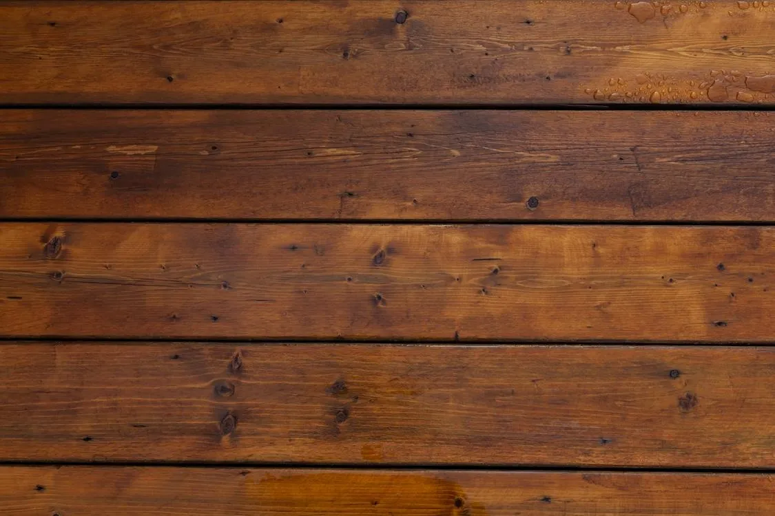 Freshly sealed wooden deck boards after maintenance, showcasing the vibrant wood grains and water beads on surface.