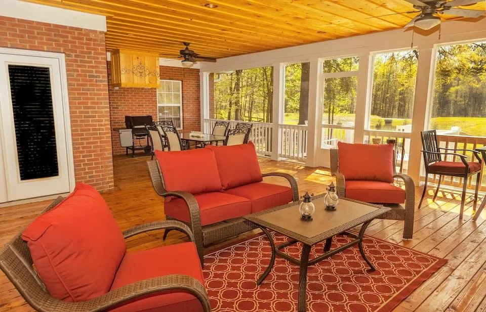 Screened porch with red cushioned furniture and a ceiling fan, overlooking a tranquil wooded backyard, illustrating Skyline Decks' expert deck construction and outdoor living space design.