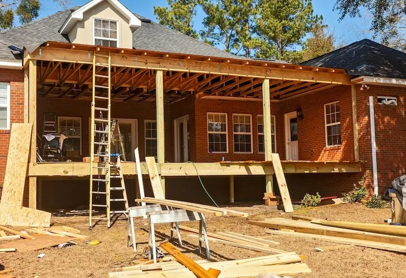 Construction of new residential deck in progress with visible wooden beams and ladder on sunny day.