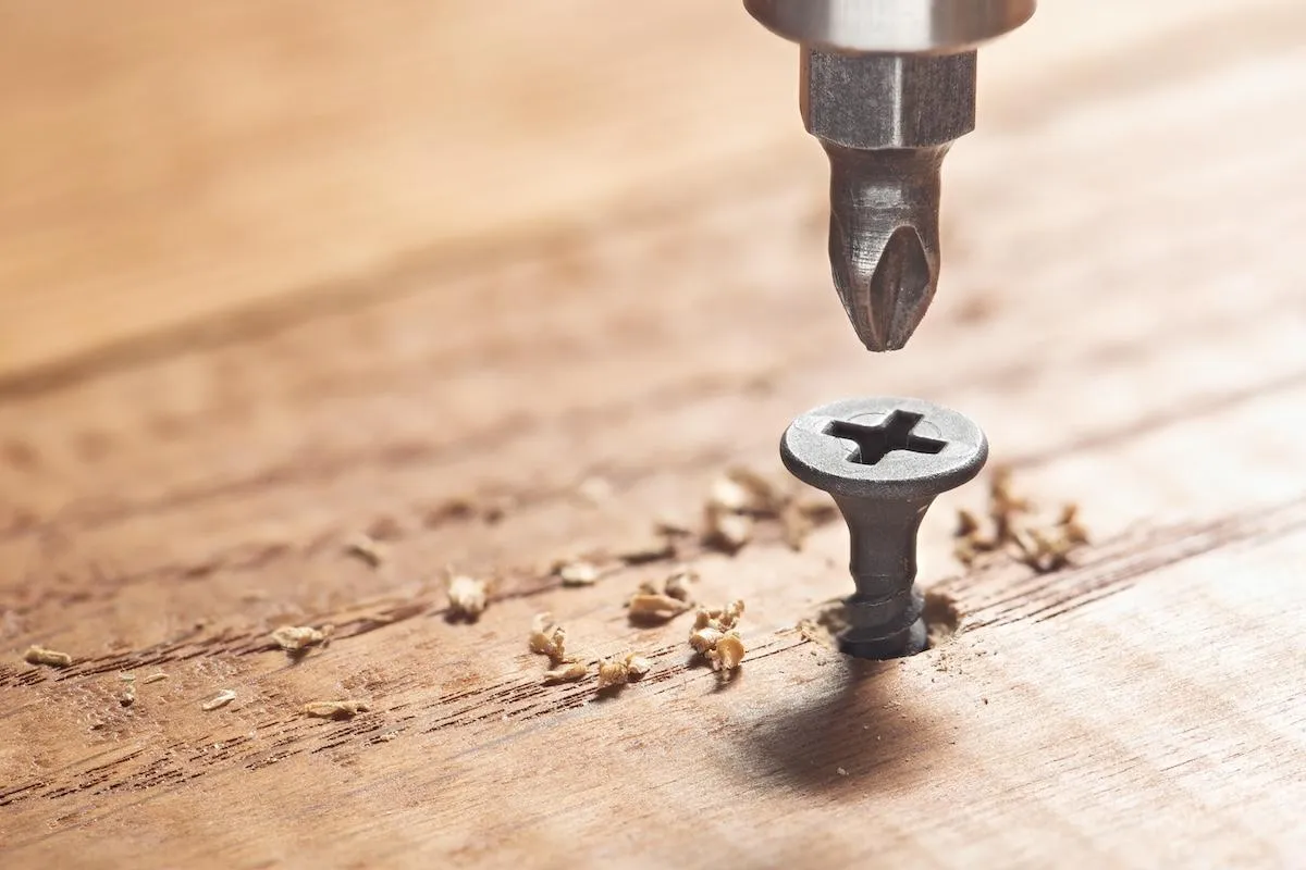 Close-up view of a power drill driving a screw into a wooden deck, showcasing precise deck construction services.