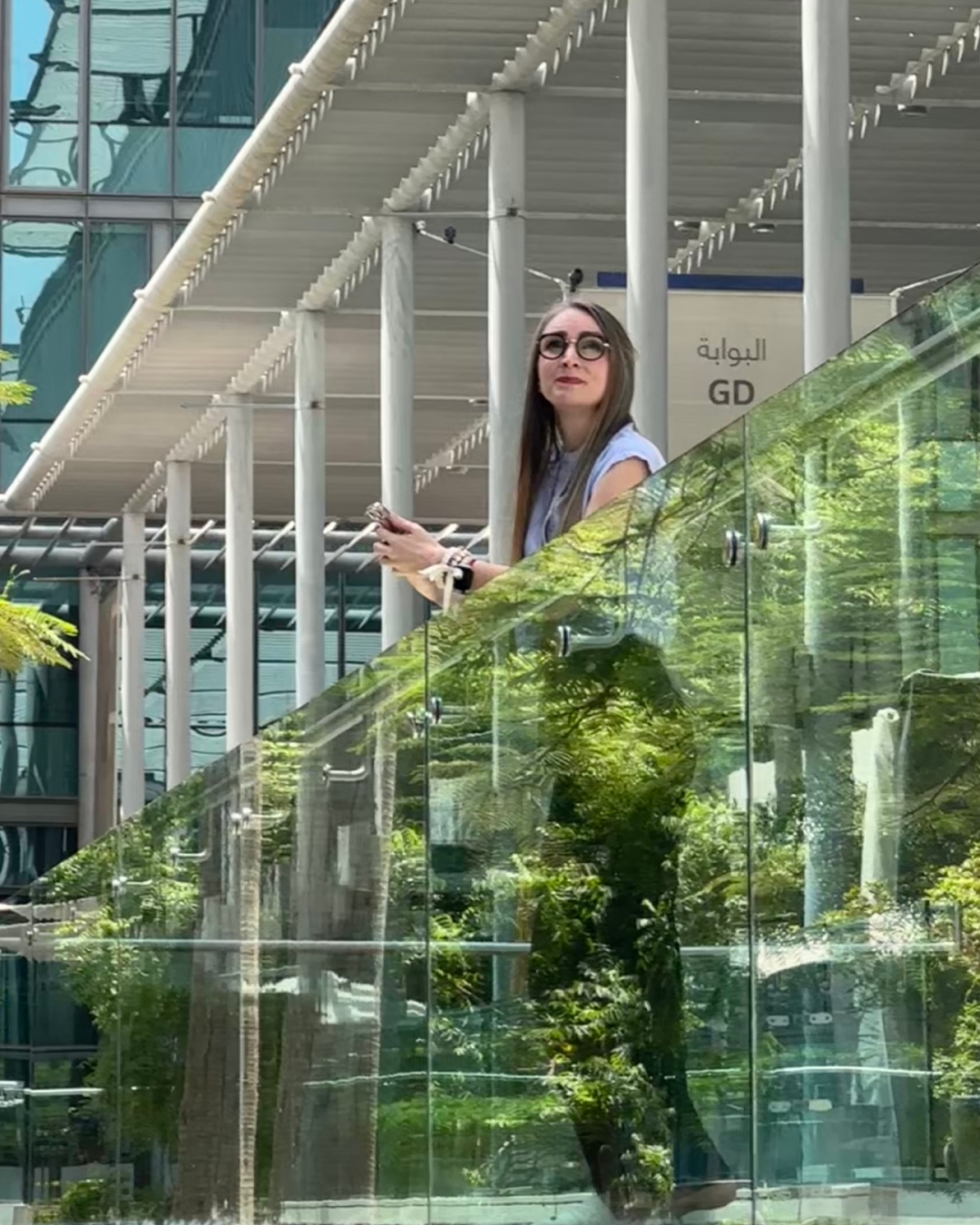 Martina Kikic standing on glass balcony in Dubai business district LinkedIn visibility coach and founder of The Peace OS