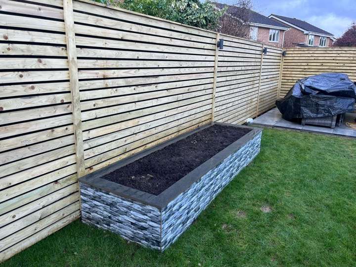 Stone-clad raised planter bed with horizontal slatted fence and turf lawn — garden project in Berkshire
