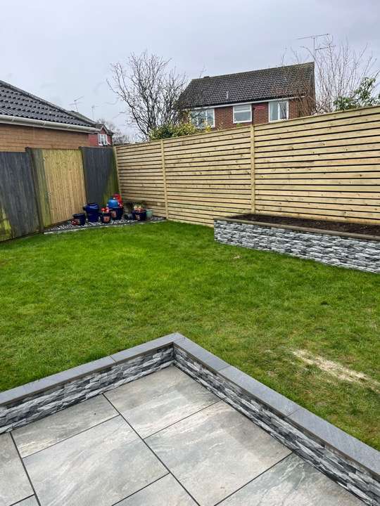 Completed garden with porcelain patio, stone-clad raised borders, turf and slatted fence — landscaping project in Reading