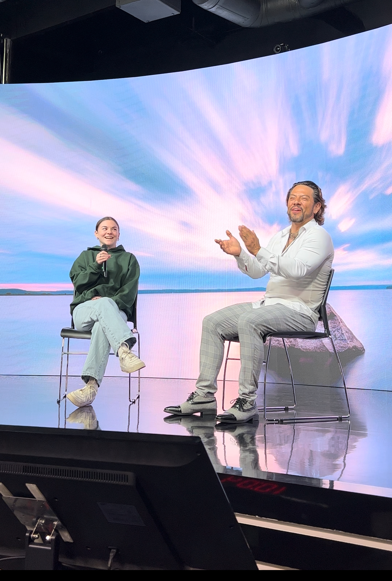 Jade Sprake working on a laptop and digital tablet while sitting on a white sofa in a pink striped shirt.