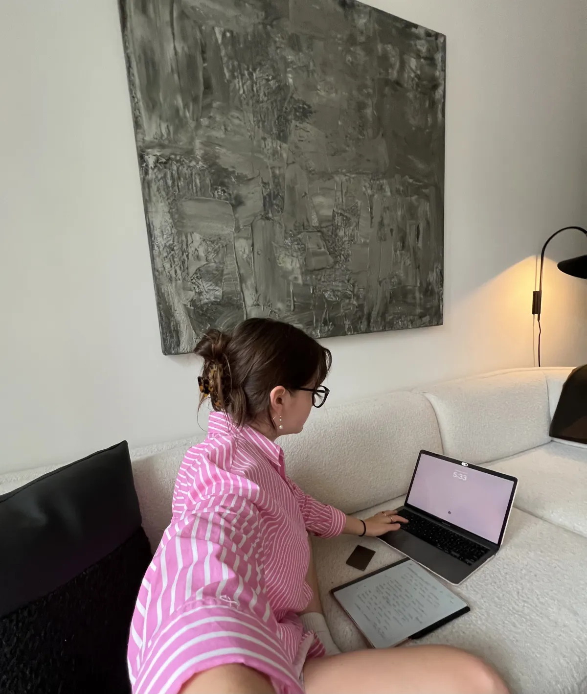 Jade Sprake working on a laptop and digital tablet while sitting on a white sofa in a pink striped shirt.