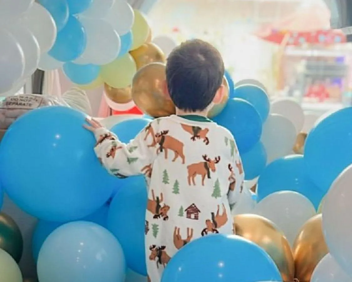 Child surrounded by colorful balloons at a birthday party featuring balloon décor and cake design.