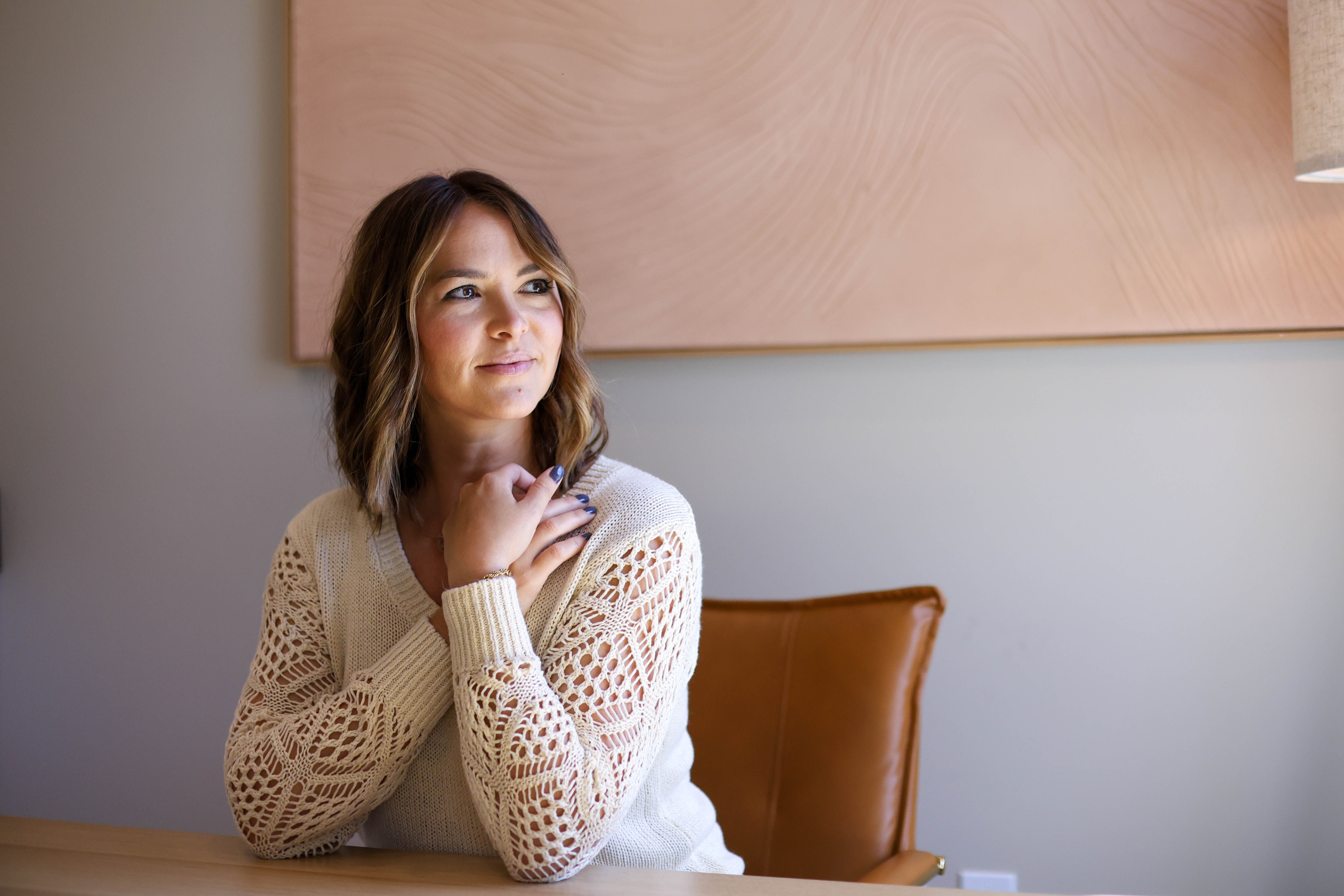 A confident woman in her 30s sits at a sunlit kitchen table, journaling with a gentle smile, surrounded by fresh fruit and a glass of water. The scene is bright, modern, and welcoming, evoking calm and empowerment.