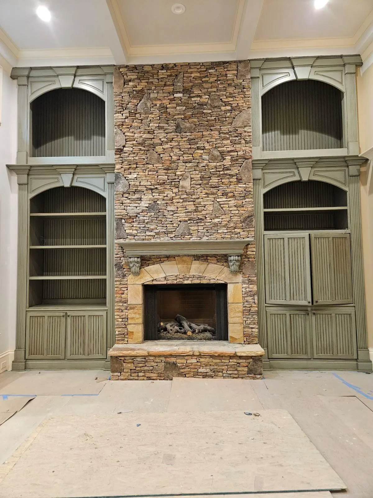 Custom built-in shelving with a unique greenish-gray limewash finish surrounding a rustic stone fireplace