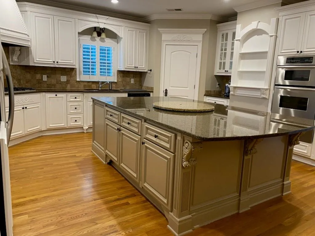 A traditional gourmet kitchen with off-white cabinets, a large central island, and dark granite countertops.