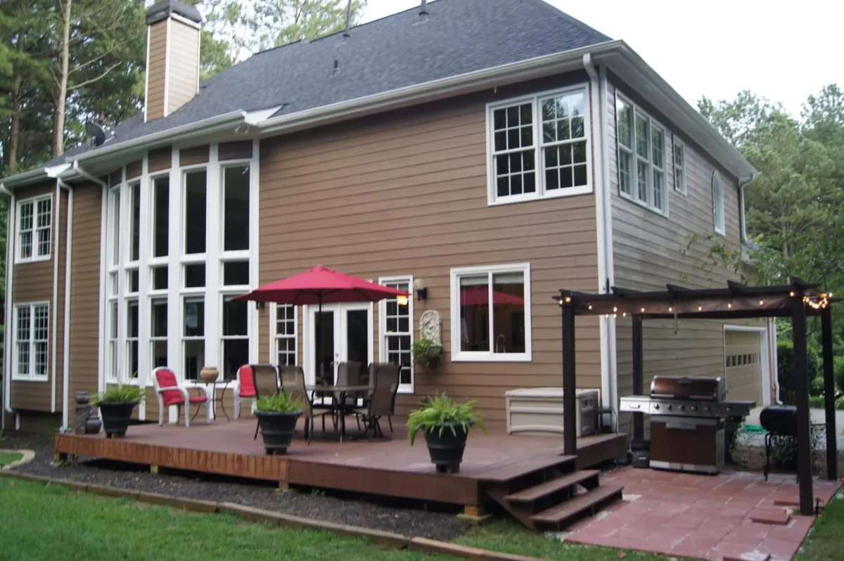 The back of a two-story home with warm brown siding and a large wooden deck complete with outdoor furniture.