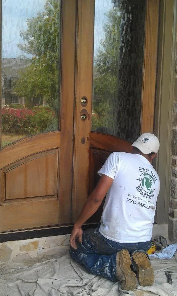 A craftsman carefully applies stain to a wooden front door, highlighting our wood finishing expertise.