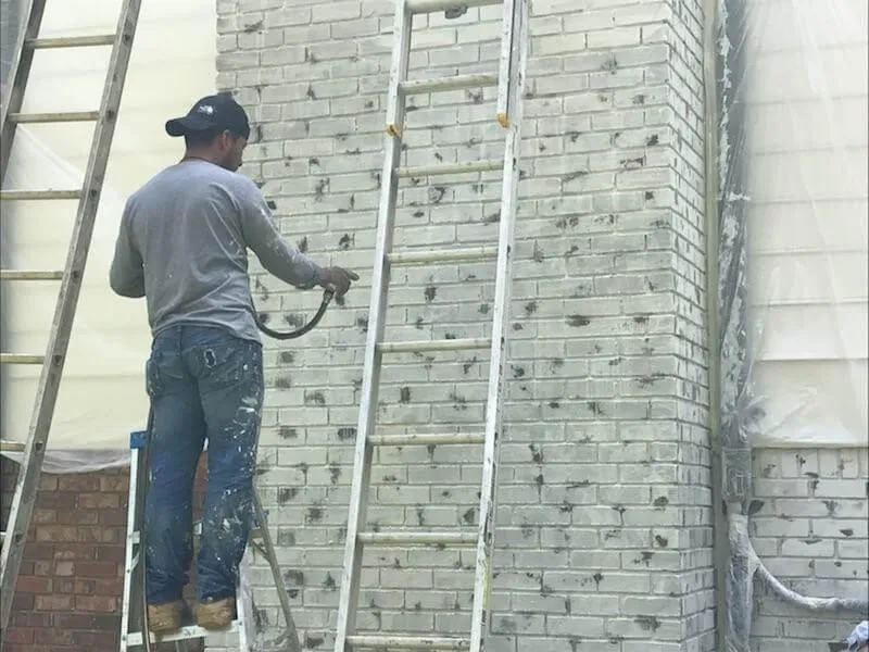 Professional painter applying a coat of white masonry paint to a red brick home in Johns Creek during a brick painting project.