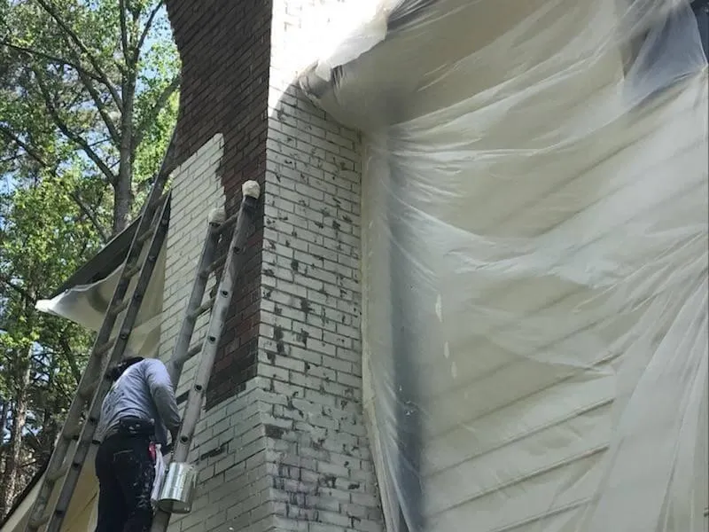 Earthly Matters technician lightly cleaning a brick wall in preparation for an authentic limewash application in Roswell.