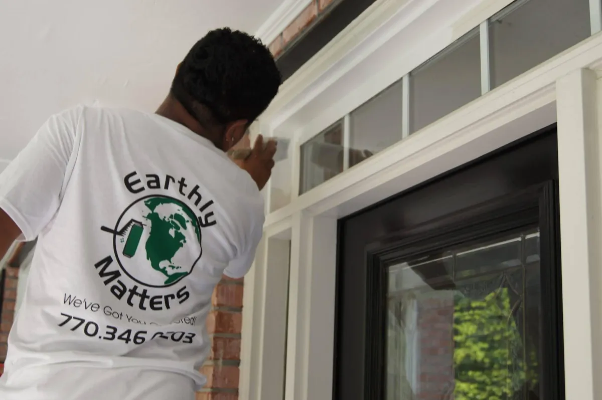 Painter on a ladder painting the exterior of a two-story brick and siding house.