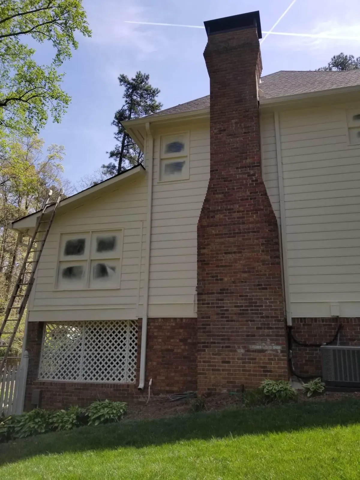 Side view of a home showing a large red brick chimney and yellowed siding before being painted.