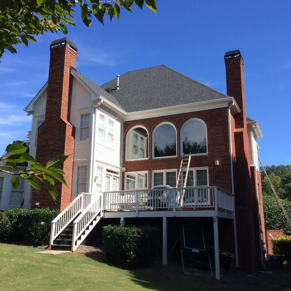 The rear view of a large red brick home, showcasing a clean white painted deck, railings, and trim.