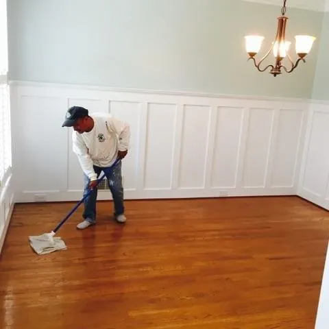A member of our crew prepping a room by cleaning the hardwood floors before painting the white wainscoting.