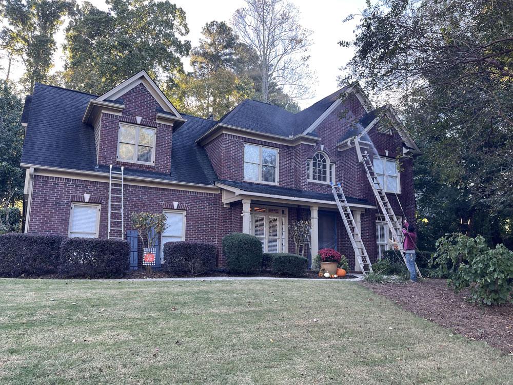 A large, dark red brick home with ladders set up, ready for its complete exterior limewash transformation