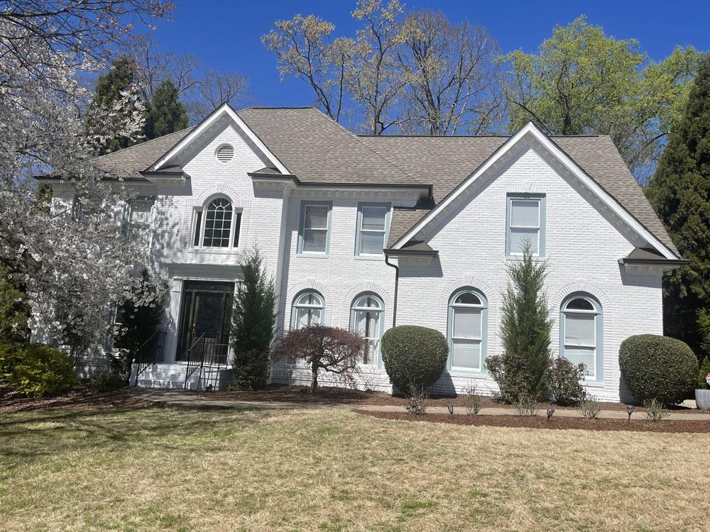 An elegant white painted brick home with unique arched windows and a clean, manicured front lawn.
