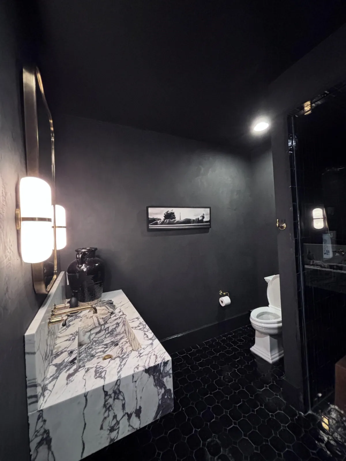 A dramatic powder room with matte black walls, a floating marble vanity, and stylish modern sconce lighting.