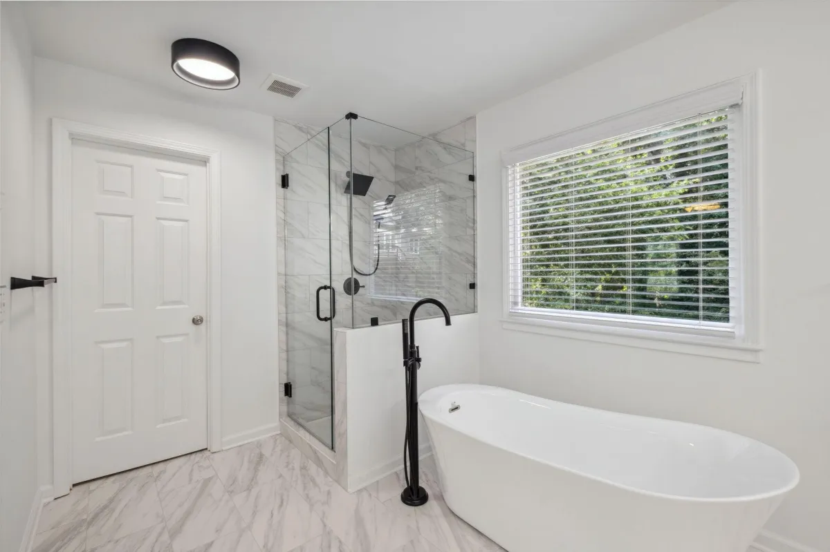 A serene bathroom featuring a white freestanding tub, black fixtures, and a glass-enclosed shower.