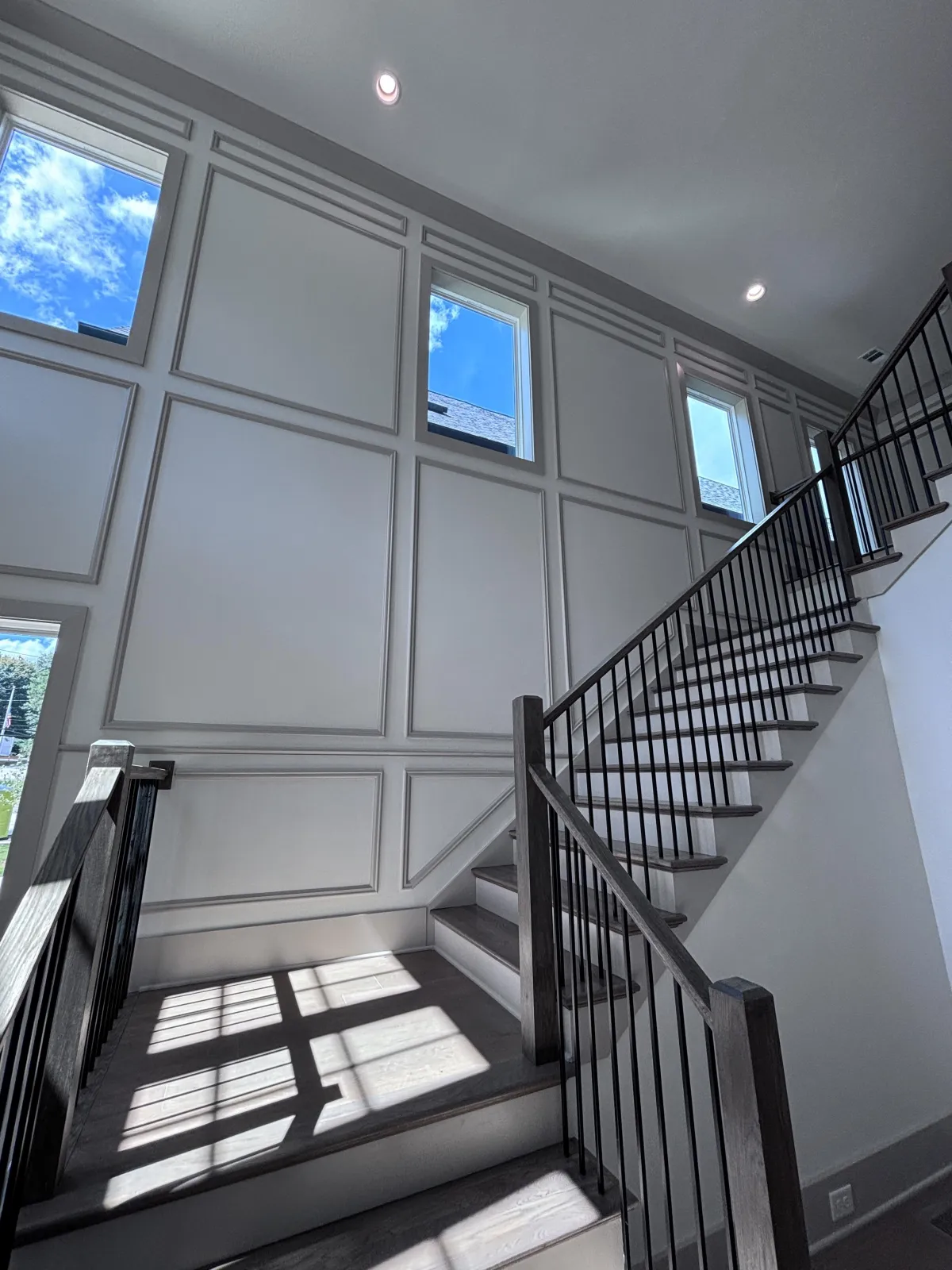 A traditional two-story foyer with standard white walls, gray decorative molding, and a classic wooden staircase.