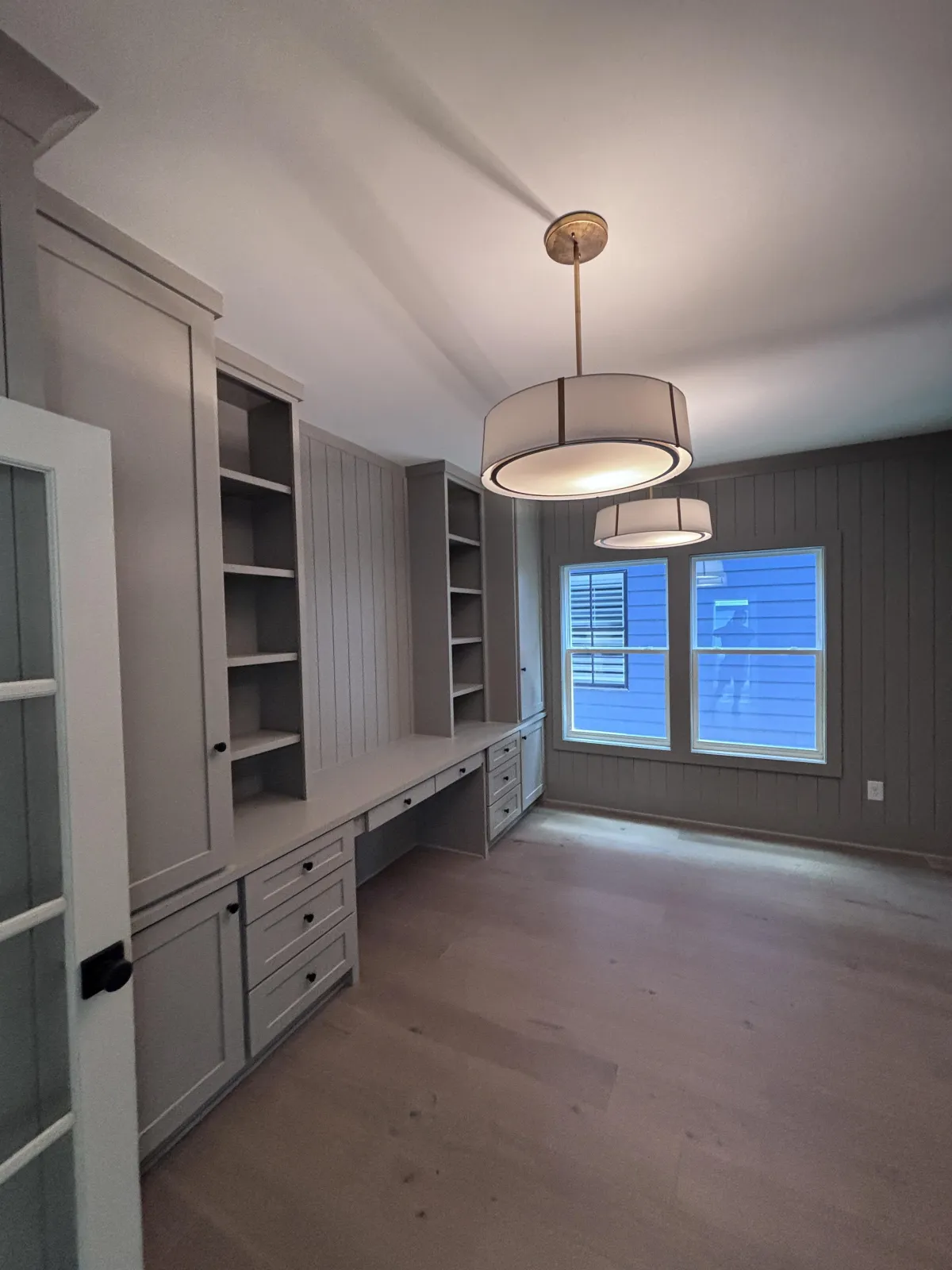 A sophisticated home office with light gray custom built-in desks, cabinets, and a dark accent wall.