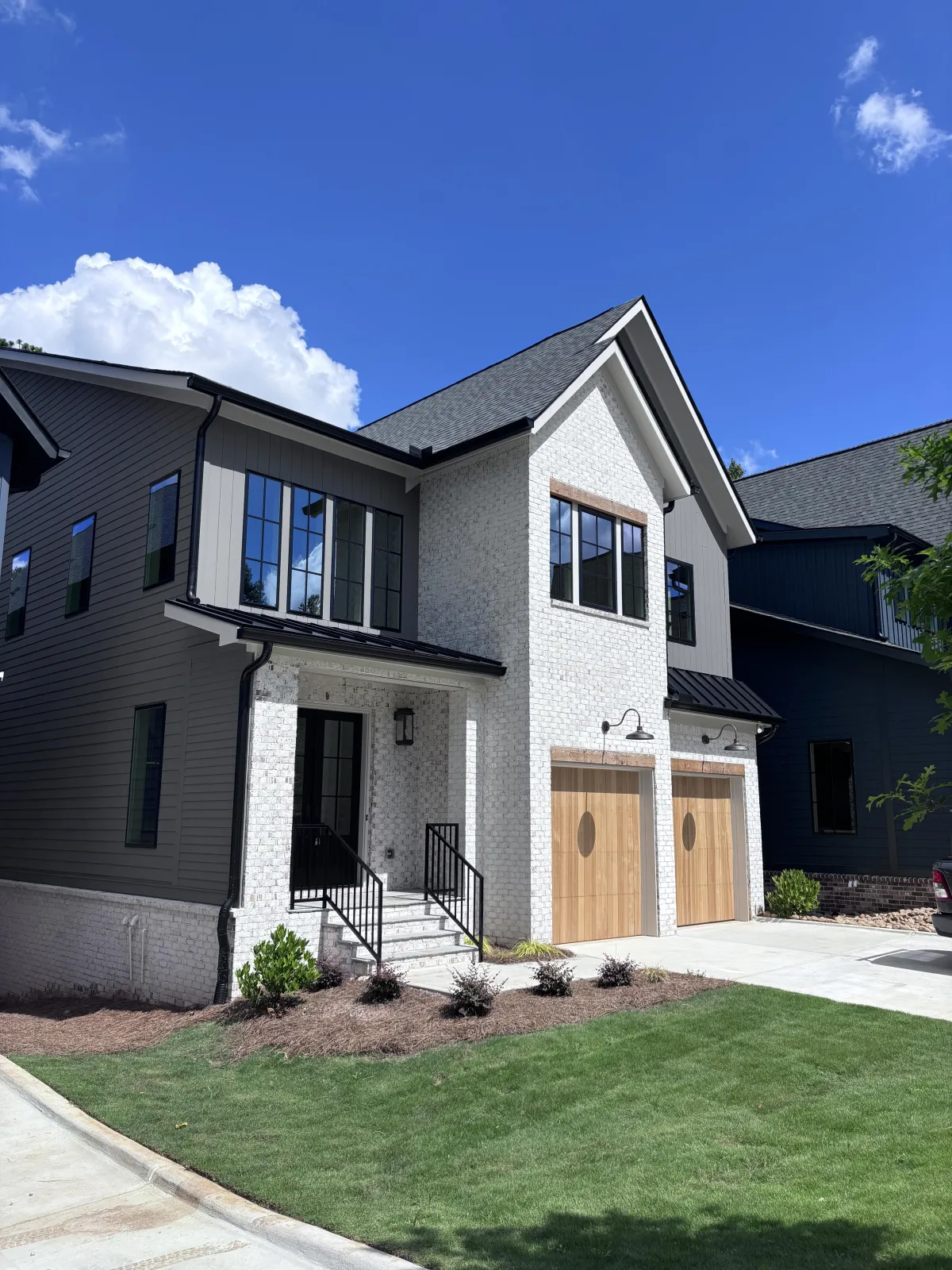 A striking modern home with a mix of materials including white textured brick, dark gray siding, and wood accents.