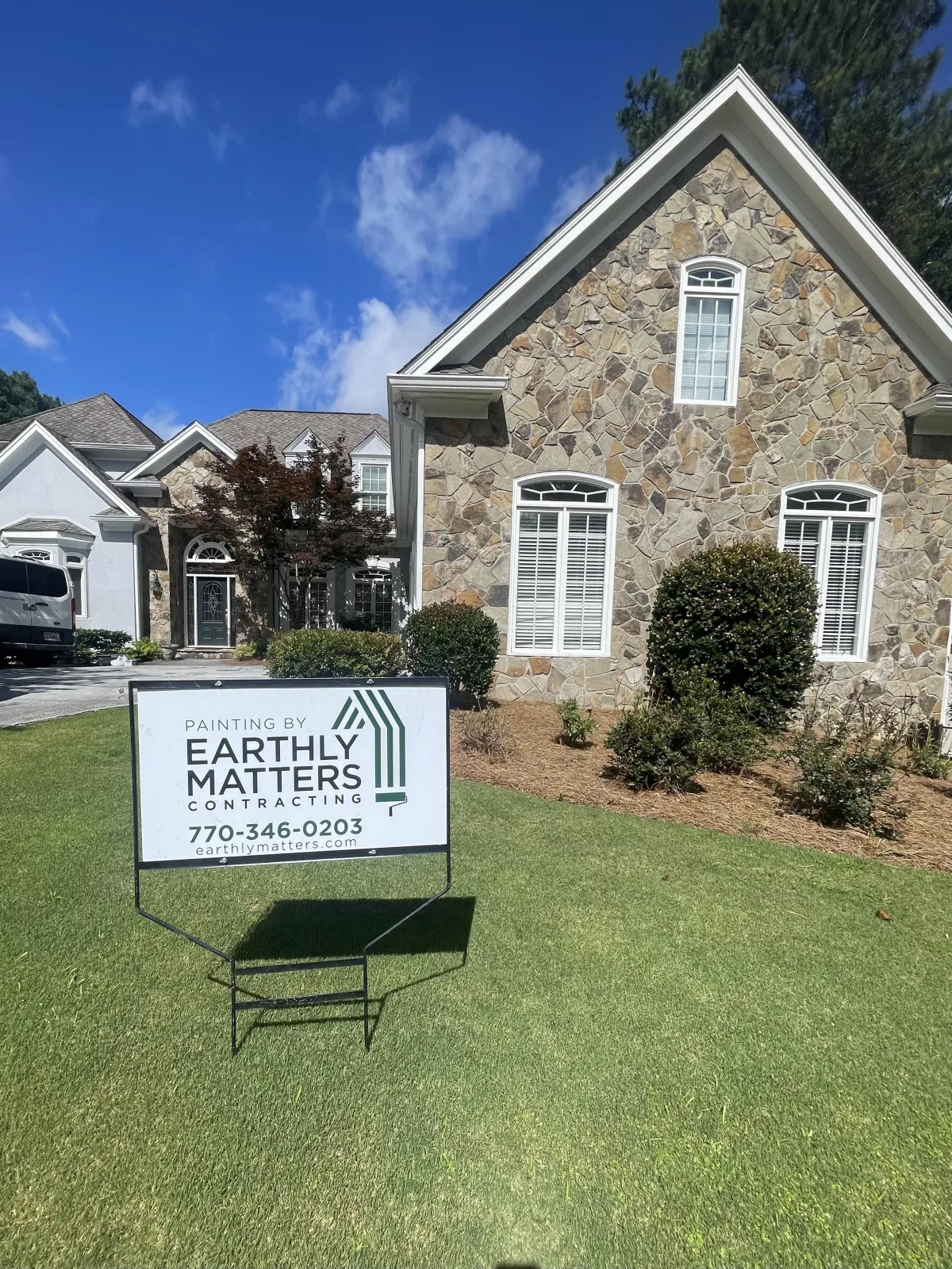 A professionally painted home with stone and siding, with a clear Earthly Matters sign displayed on the lawn.