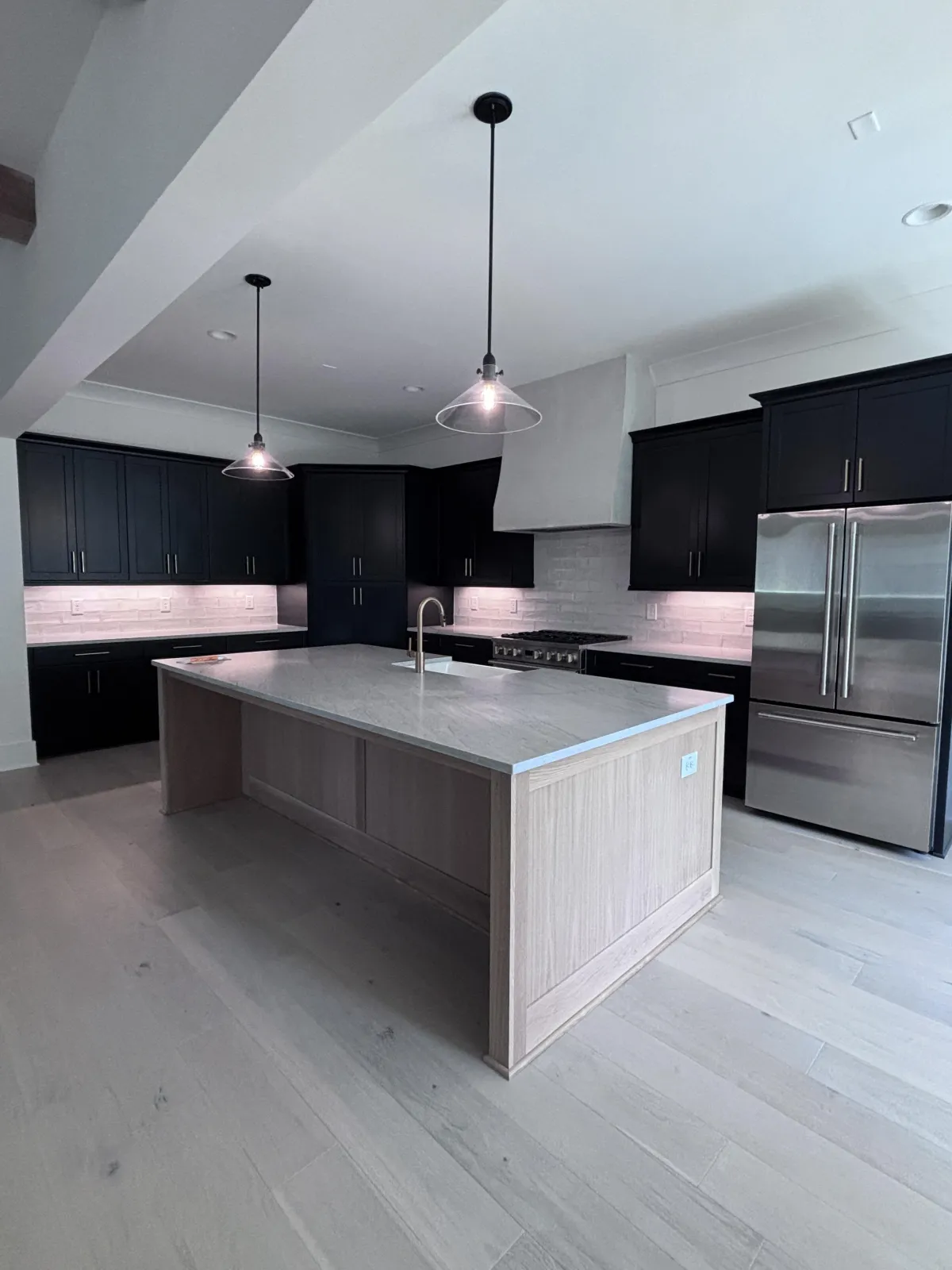 A wide view of a gourmet kitchen with dark perimeter cabinets and a large, light wood central island.