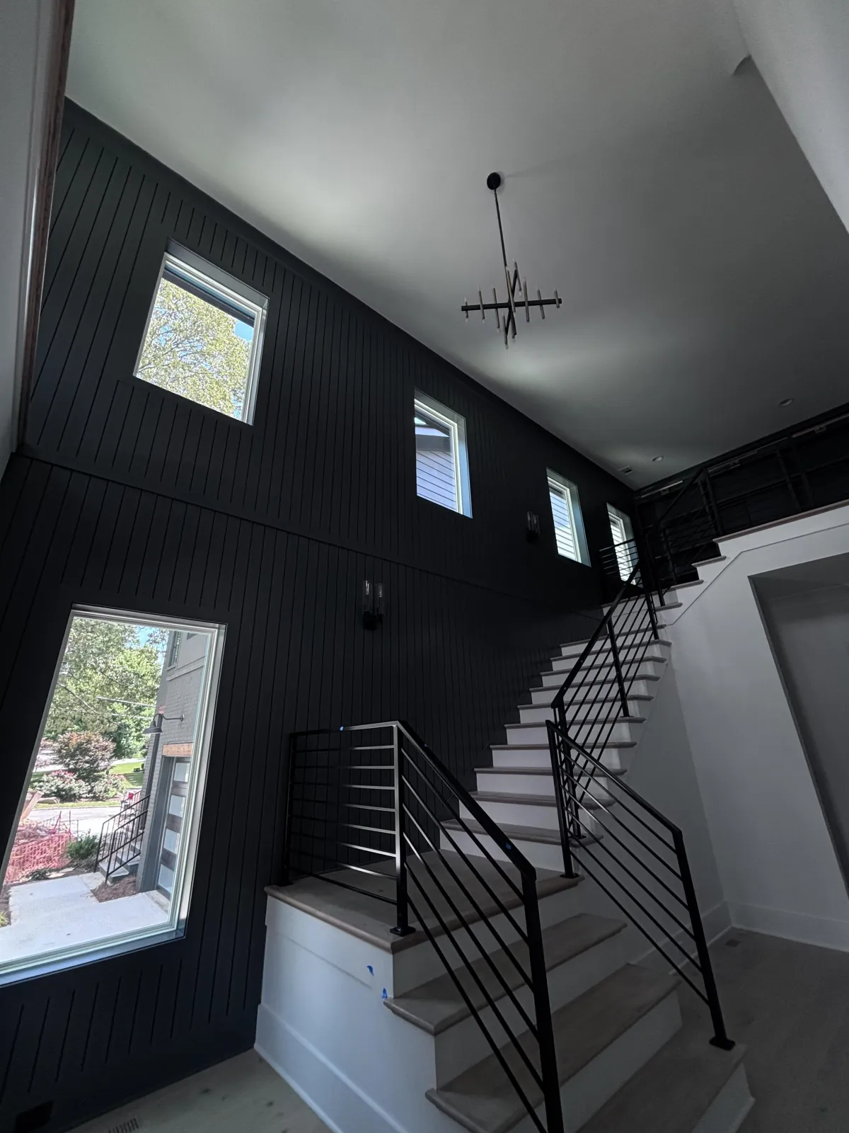 A stunning, dramatic foyer transformation featuring a bold black vertical shiplap accent wall and modern black metal railings.