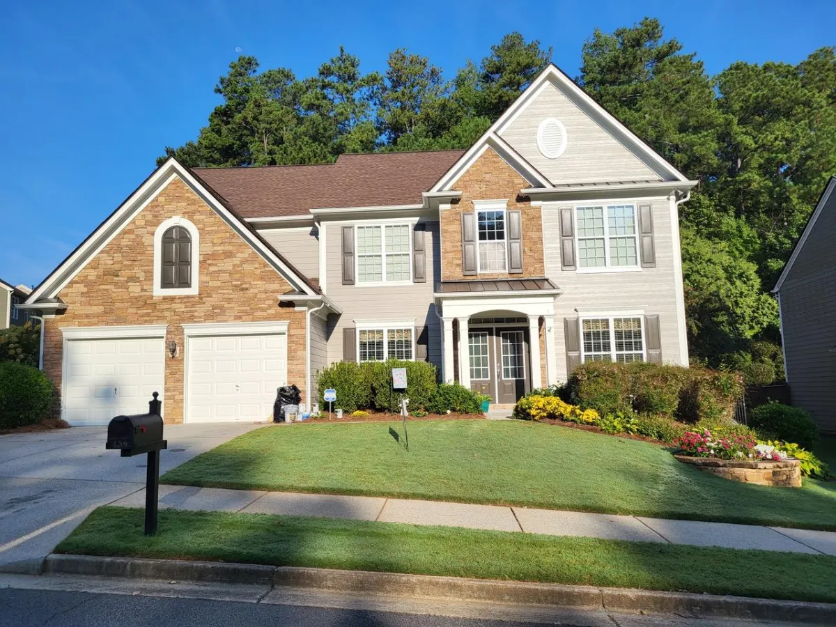 A two-story suburban home with light gray siding, a stone facade around the entrance, and a double garage.