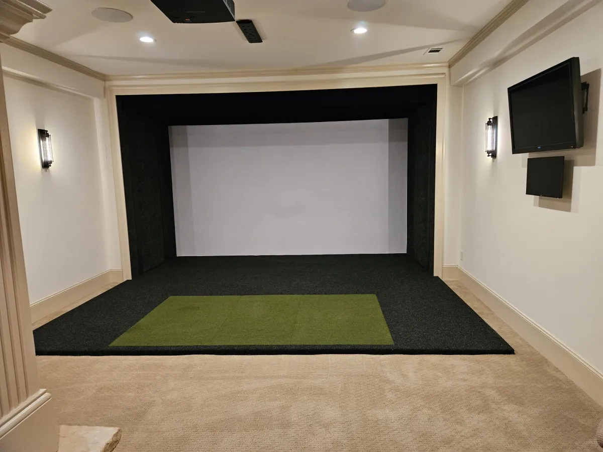 A luxury home theater room with a large projector screen, detailed trim work, and a golf simulator mat.