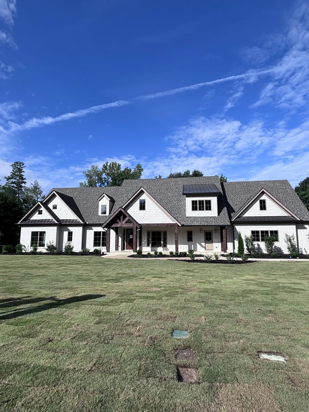 A new modern farmhouse featuring white board-and-batten siding, black trim, and natural wood garage doors.
