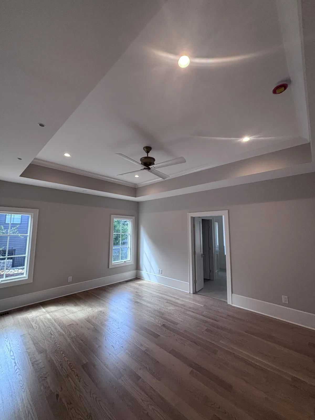 A spacious, freshly painted master bedroom with a tray ceiling, hardwood floors, and natural light.