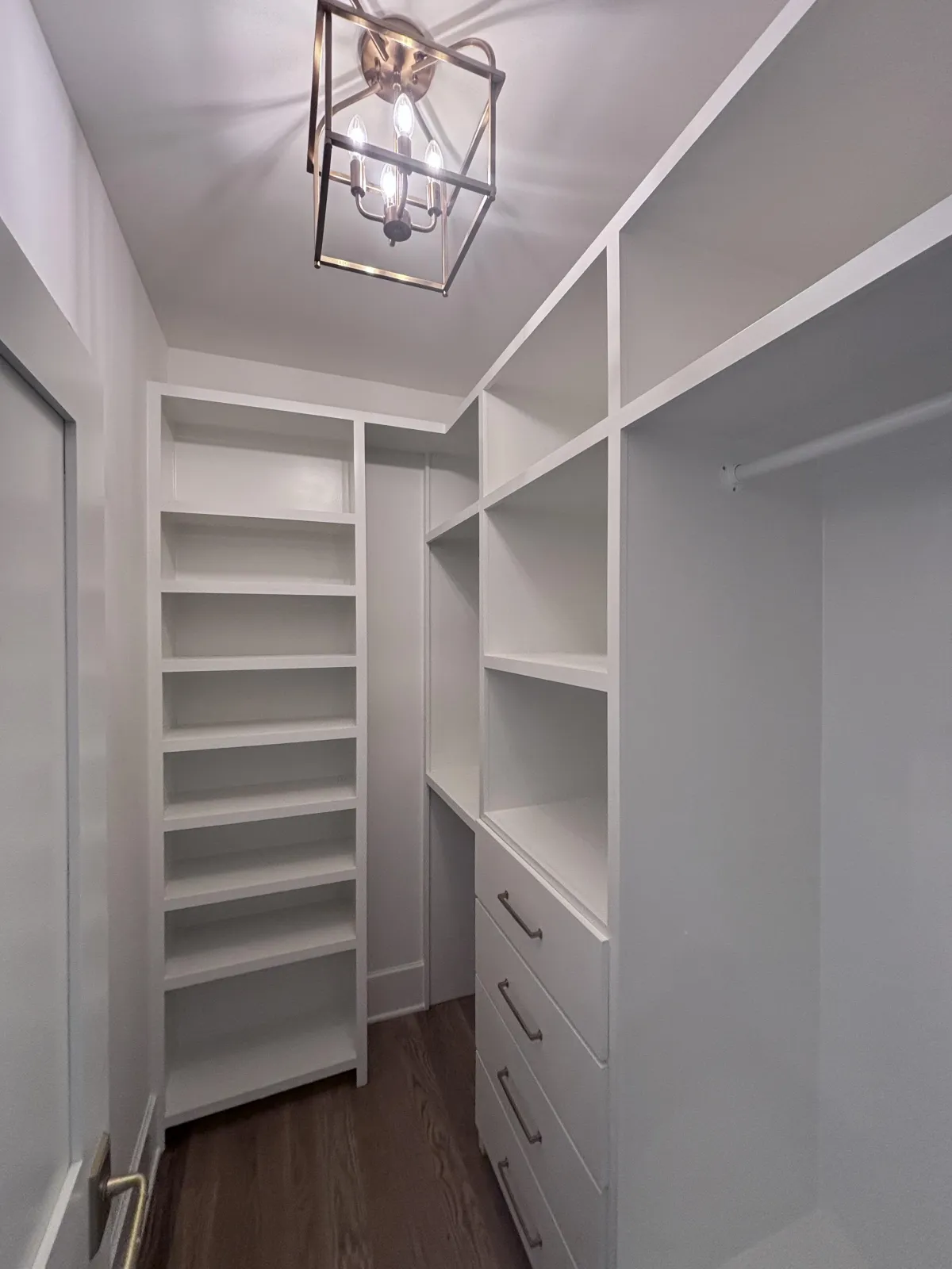 A bright white, custom walk-in closet with extensive shelving, drawers, and a modern light fixture.