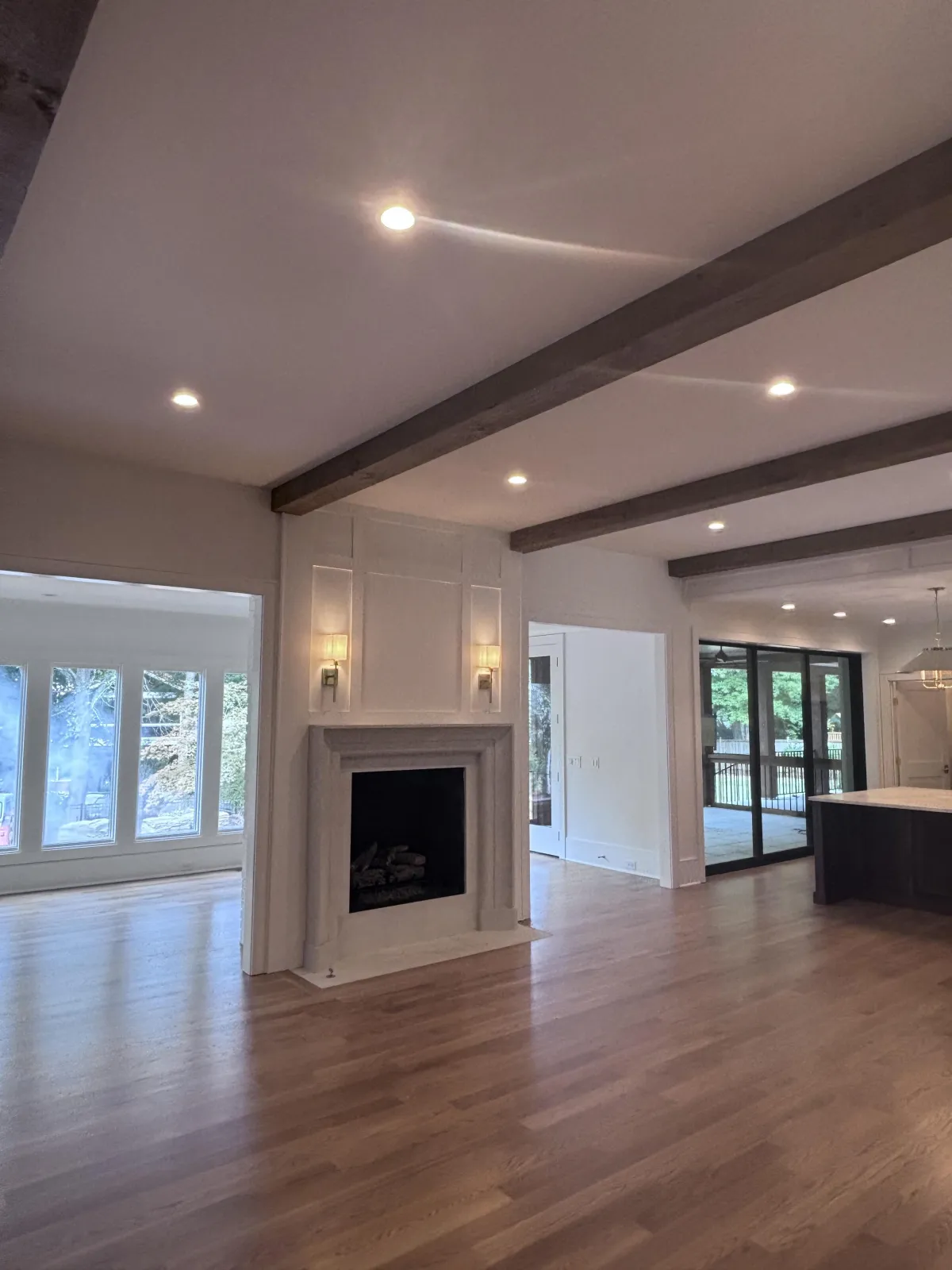 An open-concept living room centered around a white fireplace with decorative molding and rustic ceiling beams.