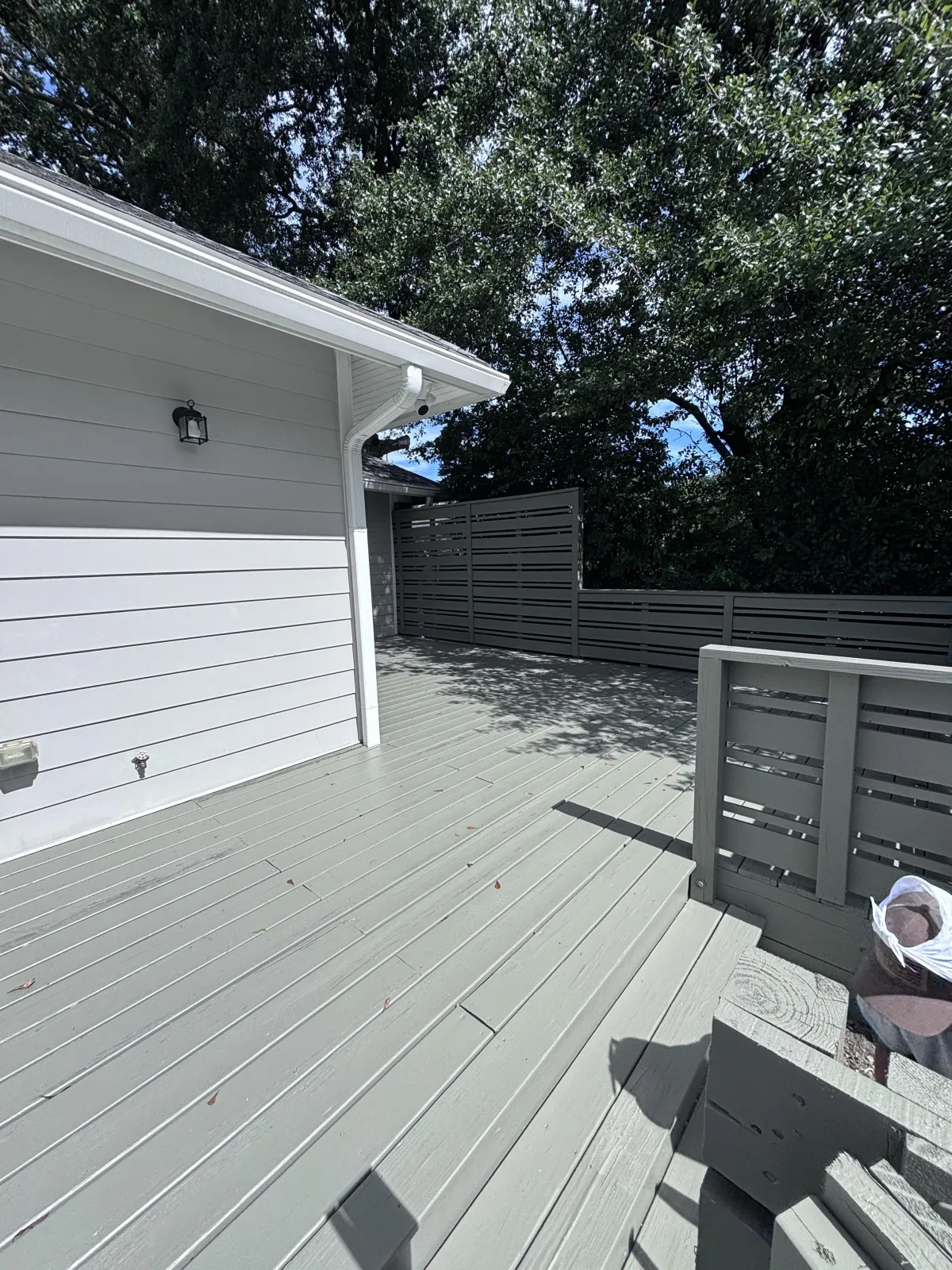 View of a newly stained wooden deck on the back of a large, light-green house.