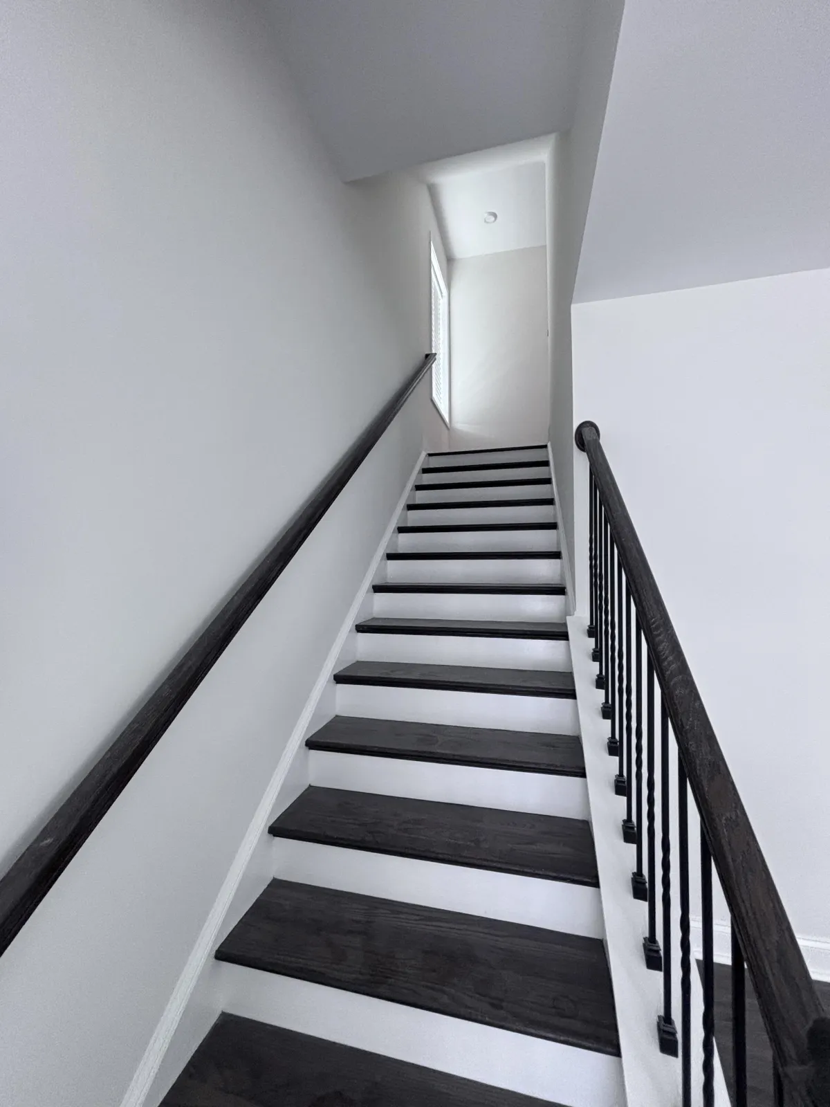 A clean, freshly painted staircase with white risers, dark wood treads, and a black metal railing.