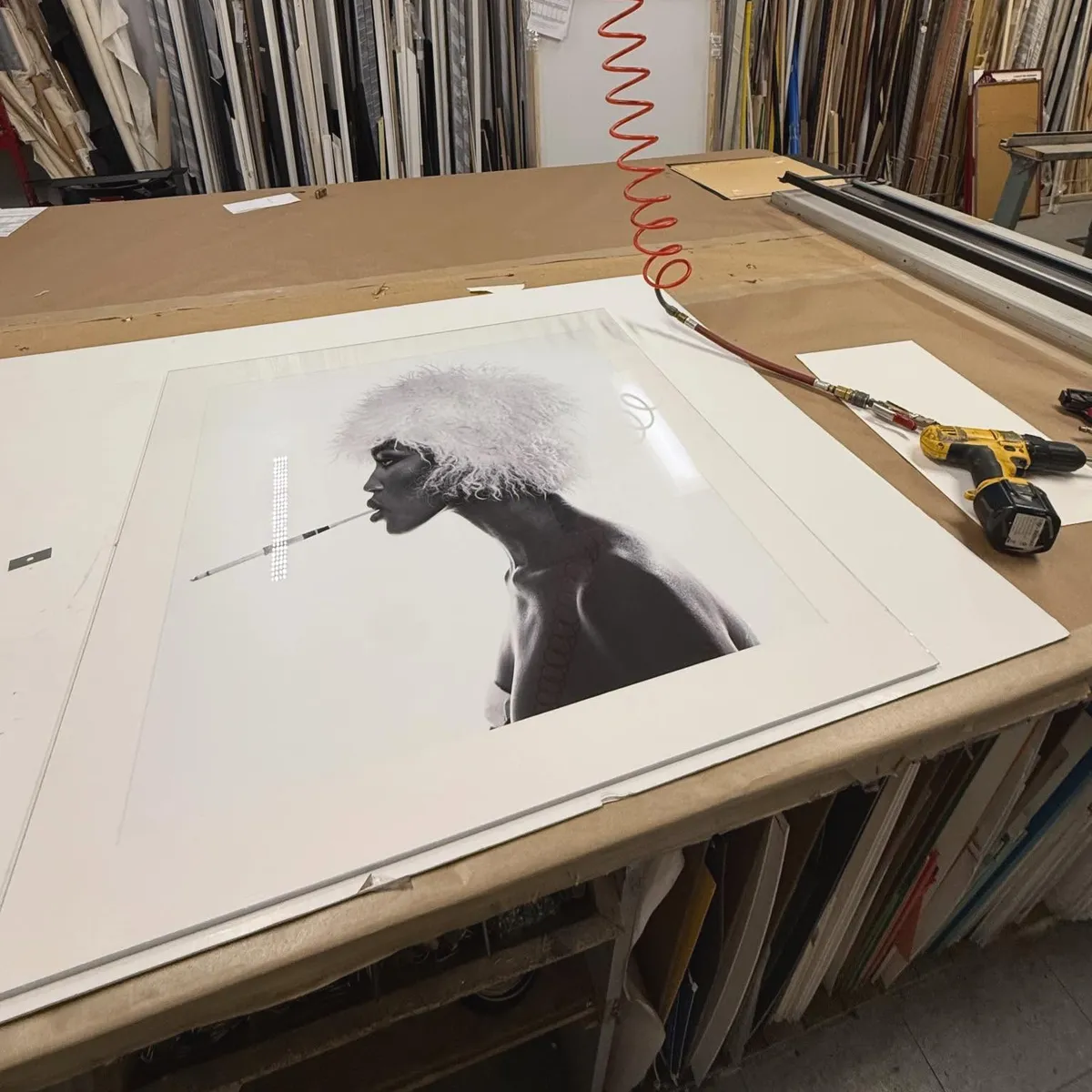Artwork being custom matted on a professional framing workbench with frame mouldings and tools visible in the background.