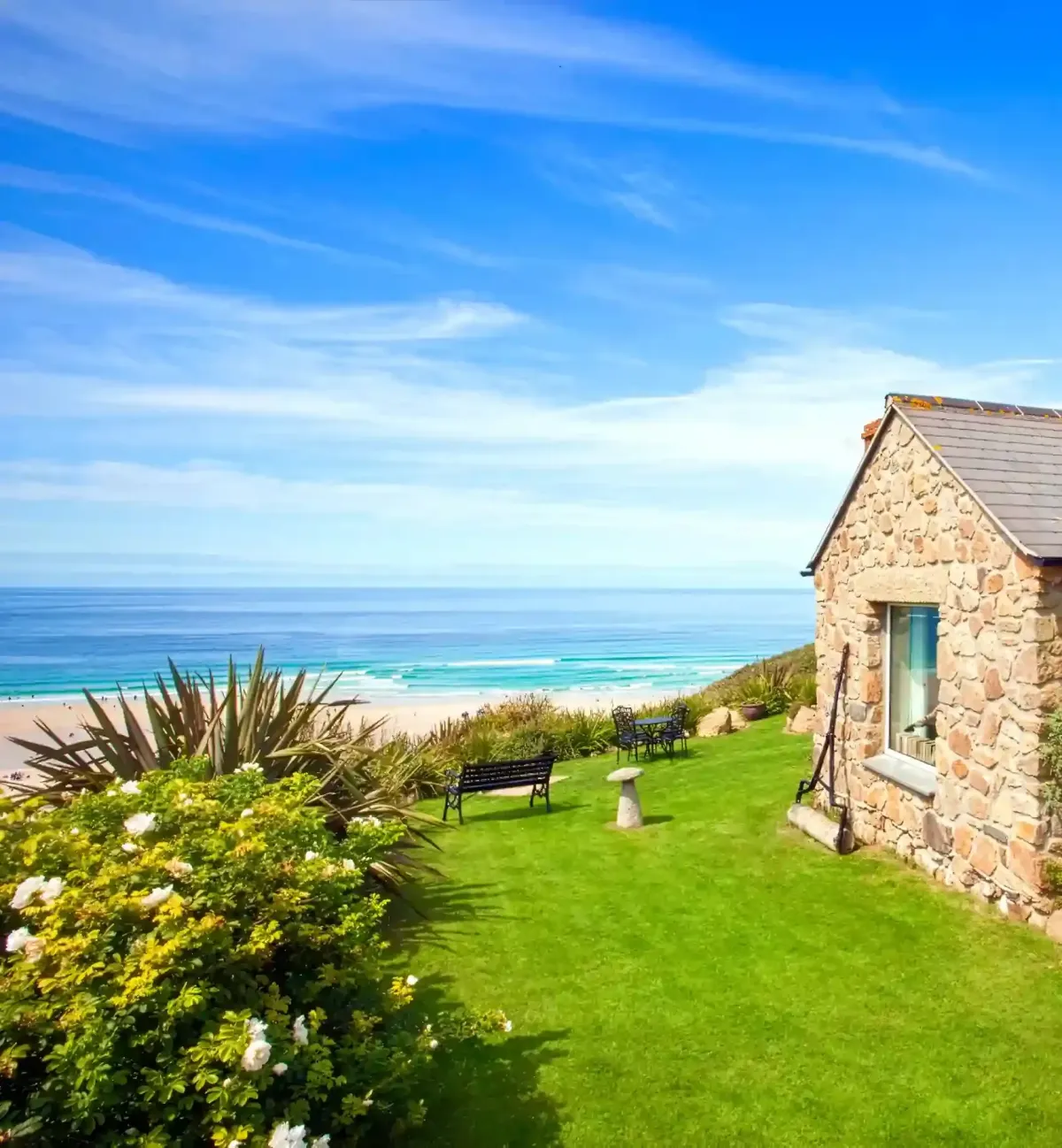  A beautiful traditional Cornish stone cottage with a lush green lawn and flowering garden, overlooking the expansive blue sea and sandy beach of Whitesands Bay, Sennen.
